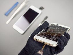 mano con guante reparando smartphone en pantalla quebrada